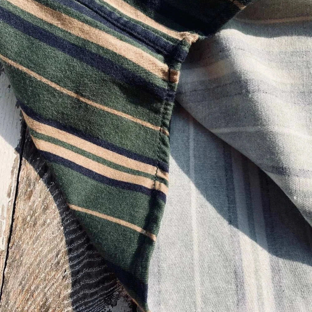 Vintage summer cotton shirt with green and beige stripes on rustic wooden surface.