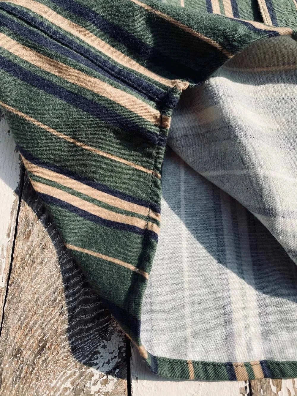 Vintage summer cotton shirt with green and beige stripes on rustic wooden surface.