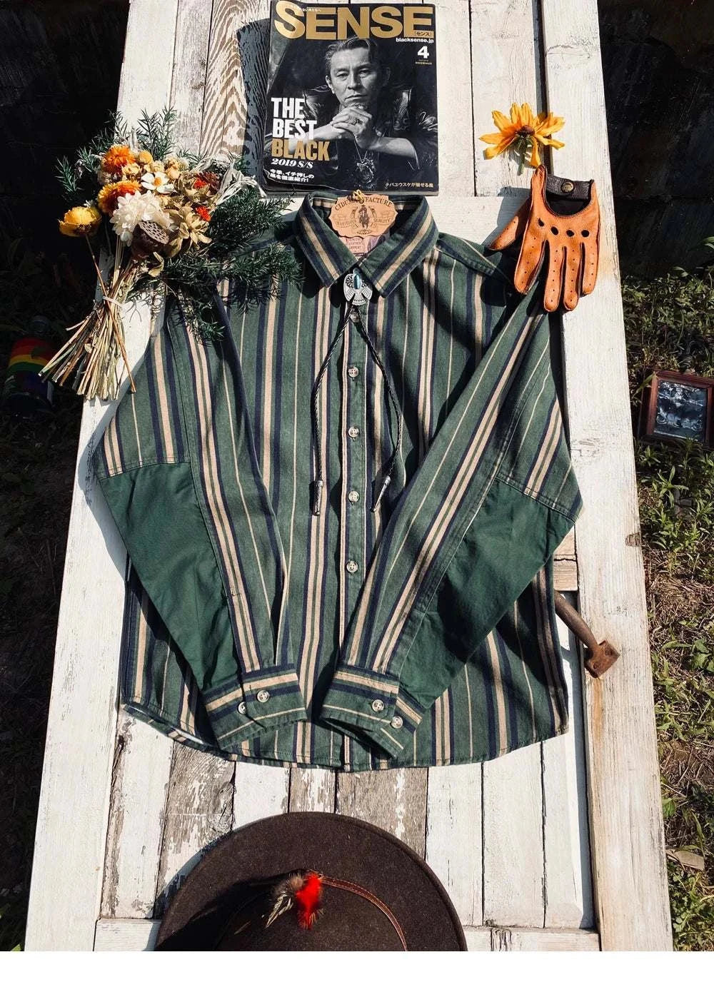 Vintage summer cotton shirt with stripes, classic collar, laid on outdoor surface with flowers and accessories.