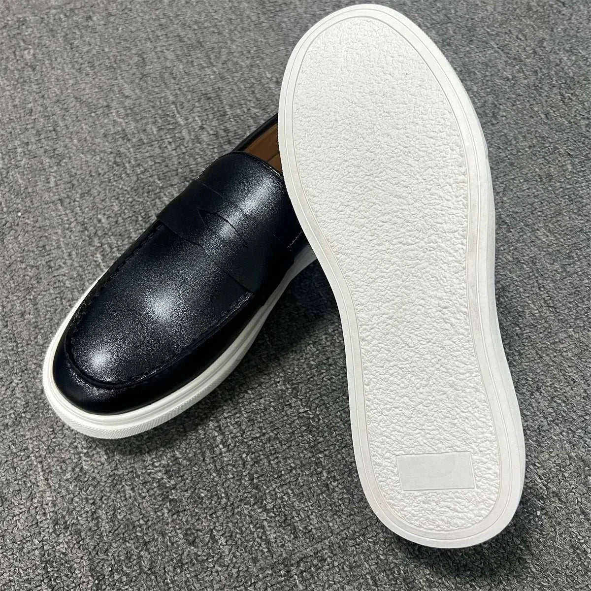 Black casual slip loafers on gray carpet, showcasing luxurious suede, elastic side panels, and white PU leather outsole.