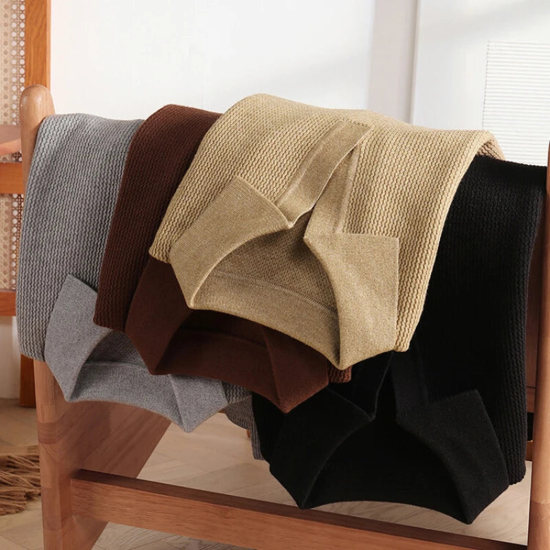Four textured blankets in gray, brown, beige, and black draped over a wooden chair.