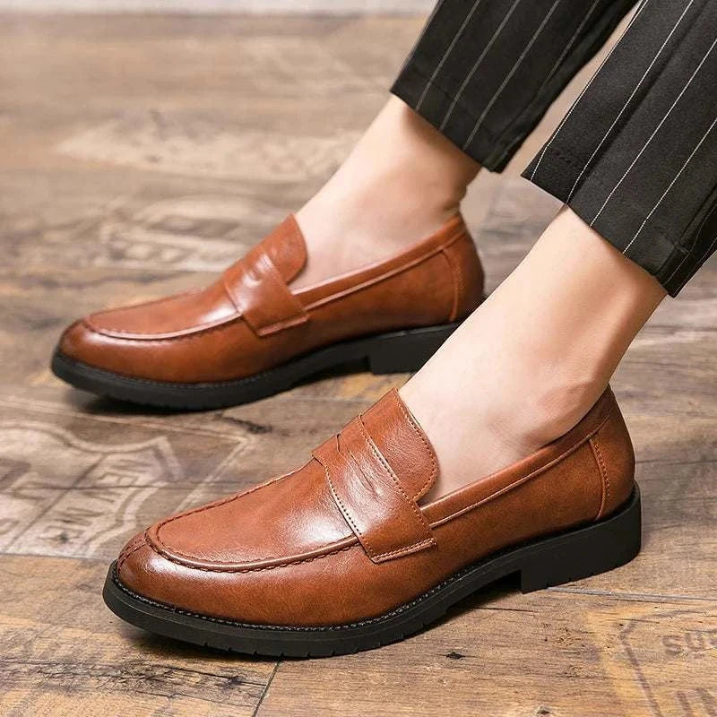 Brown British casual loafers with rubber outsole on wooden floor.