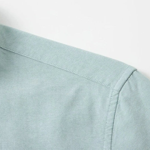 Close-up detail of a light sage green shirt showing the shoulder seam, collar, and fabric texture against a plain white background.