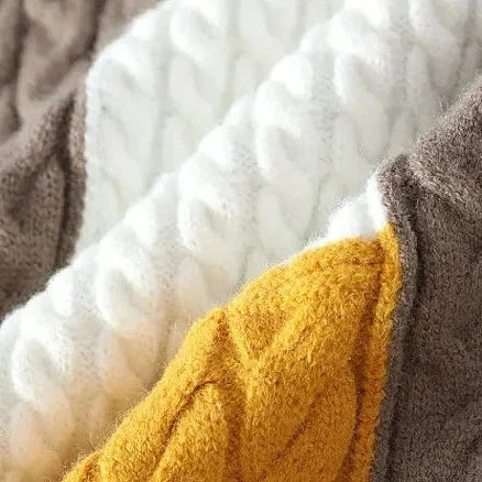 Cable-knit fabric detail of Norway neck sweater in brown, white, and yellow.