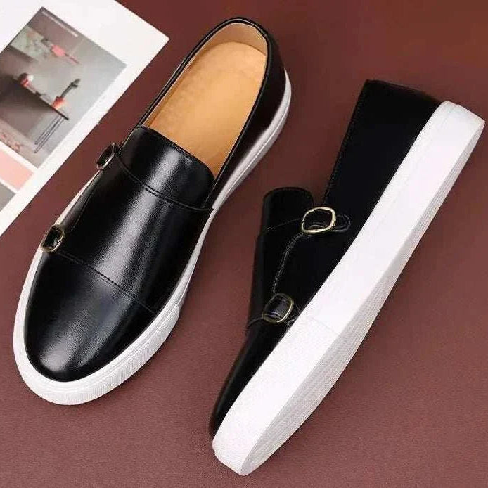 Monk British loafers in black leather with dual buckle design and white soles.