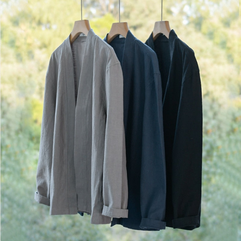 Three Antonios Linen Long-Sleeved Shirts in gray, navy, and black hanging on hangers against a blurred natural background.