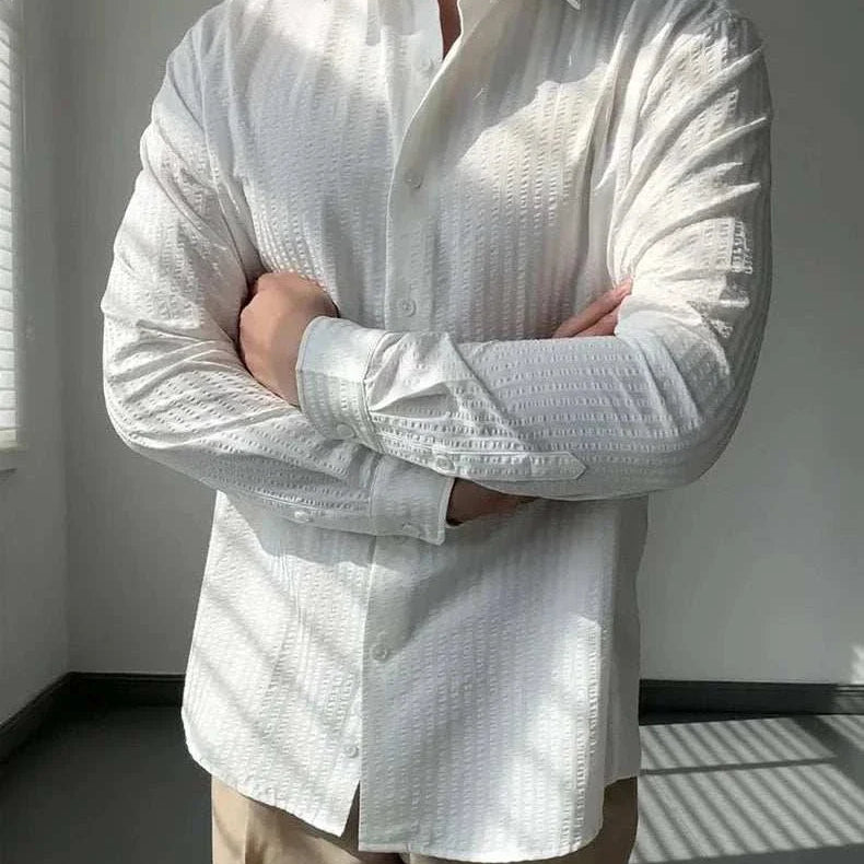 Men's white striped shirt with classic collar, Antonios British casual style, paired with beige pants in a sunlit room.