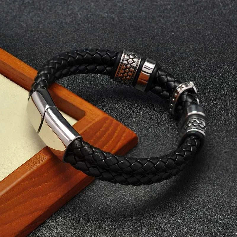Stainless steel cross magnet bracelet with black PU strap on wooden surface.