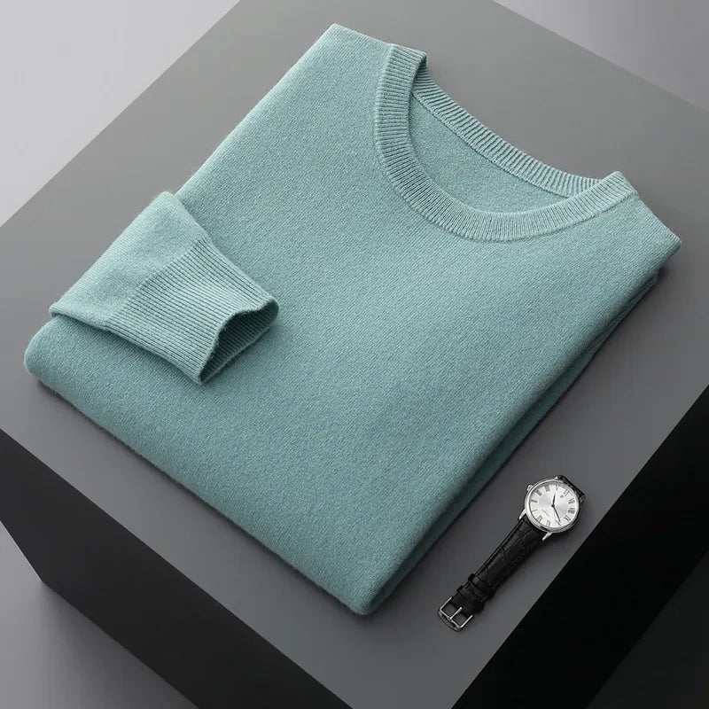 Antonios Pure Wool Sweater in turquoise, folded on a dark surface with a watch beside it.