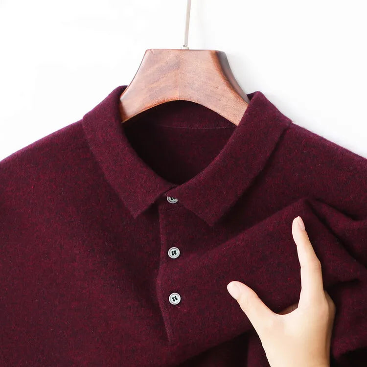 A close-up of a burgundy knit polo shirt on a wooden hanger, with a hand holding the sleeve to show the fabric texture.