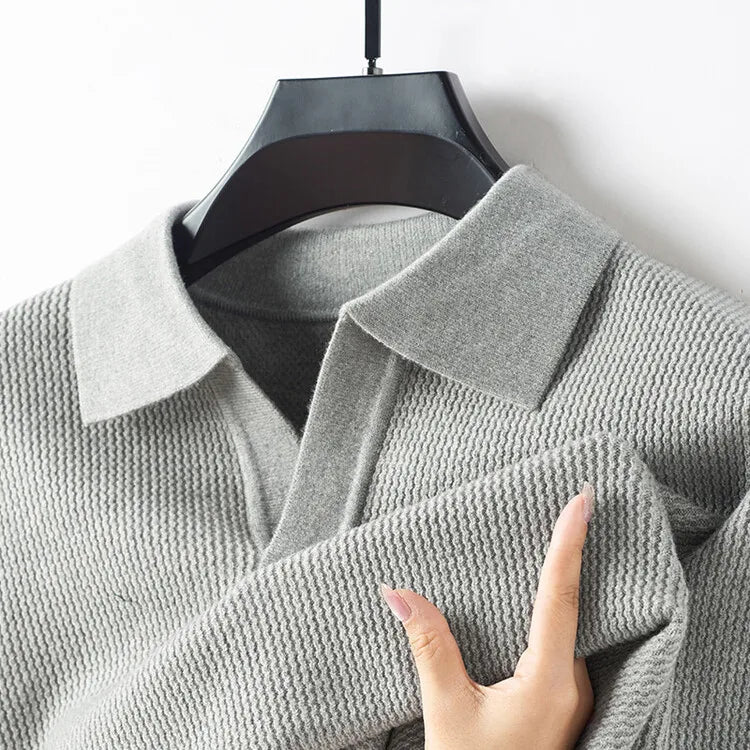 Gray textured sweater on a hanger with a hand touching the fabric