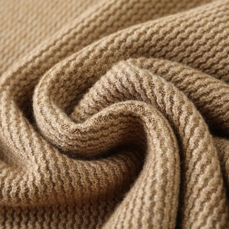 A close-up of a soft, ribbed knit fabric in a warm taupe-brown color, arranged in a gentle spiral to show the texture and drape.