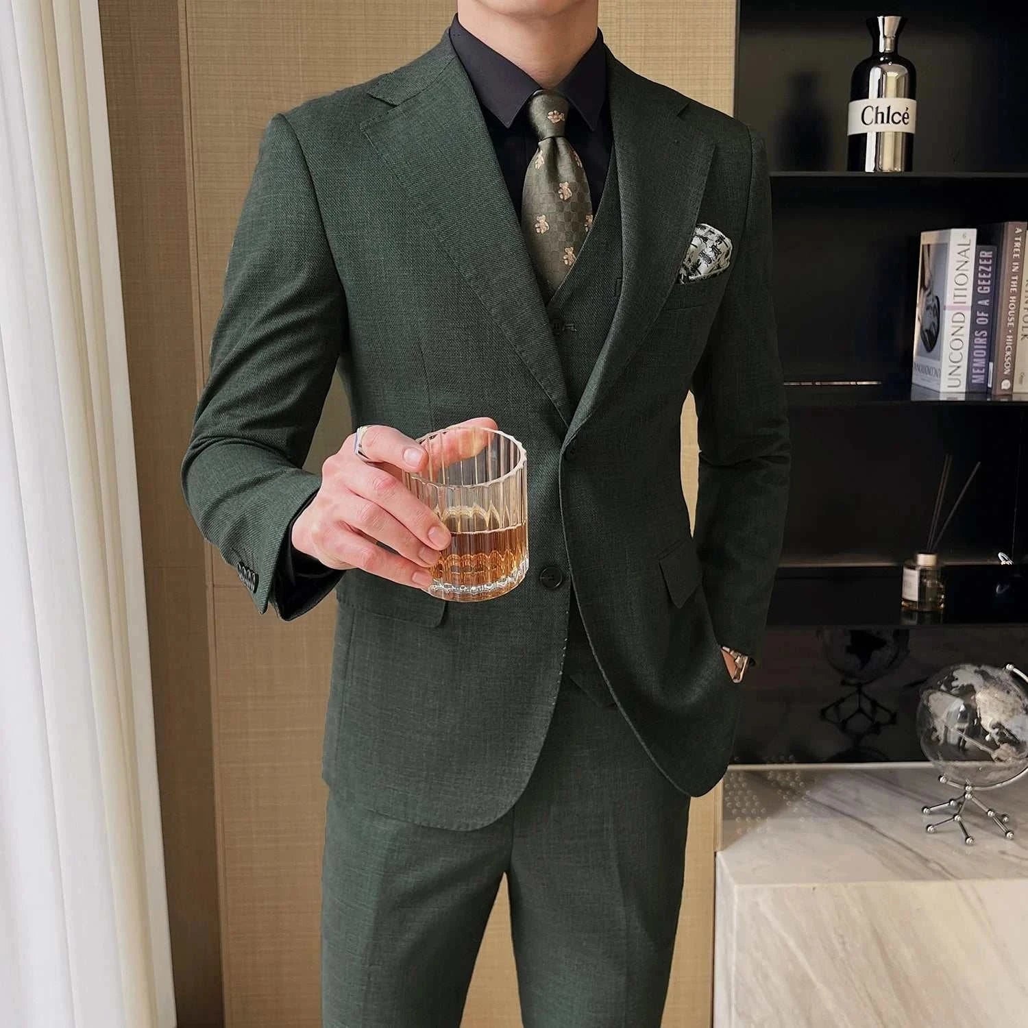 Groom in stylish green three-piece wedding suit holding a drink.