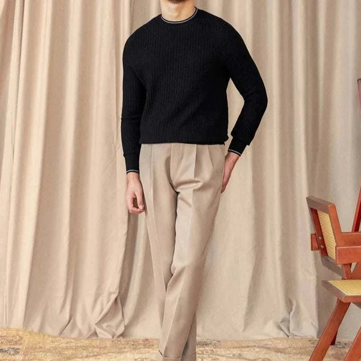 Men's winter wool sweater in black, styled with beige pants, set against a curtain backdrop.