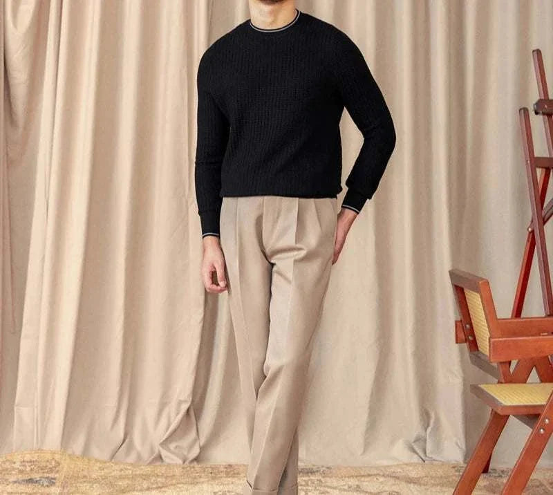 Men's winter wool sweater in black, styled with beige pants, set against a curtain backdrop.