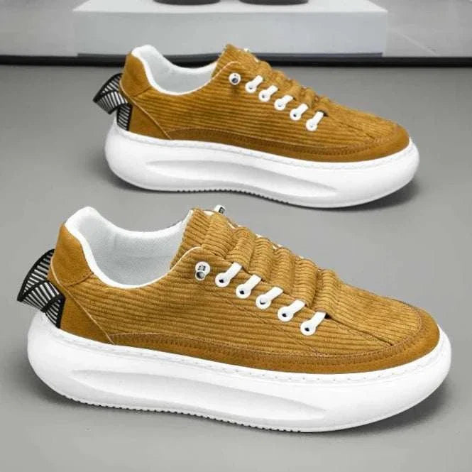 Cricket bulb shoes in mustard color with white soles placed on a gray surface.