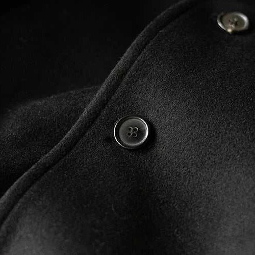 Close-up view of a single breasted trench coat button in black fabric.