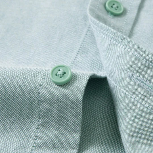 Close-up of a light sage green woven fabric garment, showing the collar, button placket, and matching green buttons.