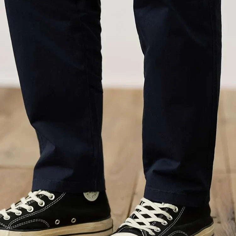 Classic chino pants in navy paired with black sneakers on wooden floor.