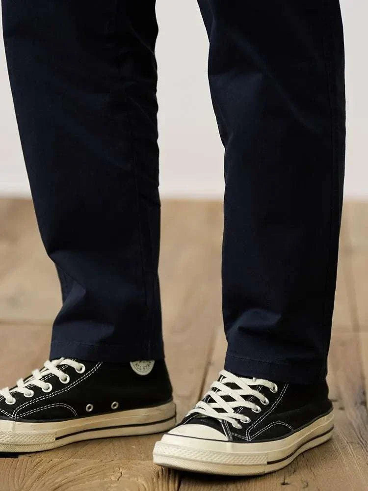Classic chino pants in navy paired with black sneakers on wooden floor.