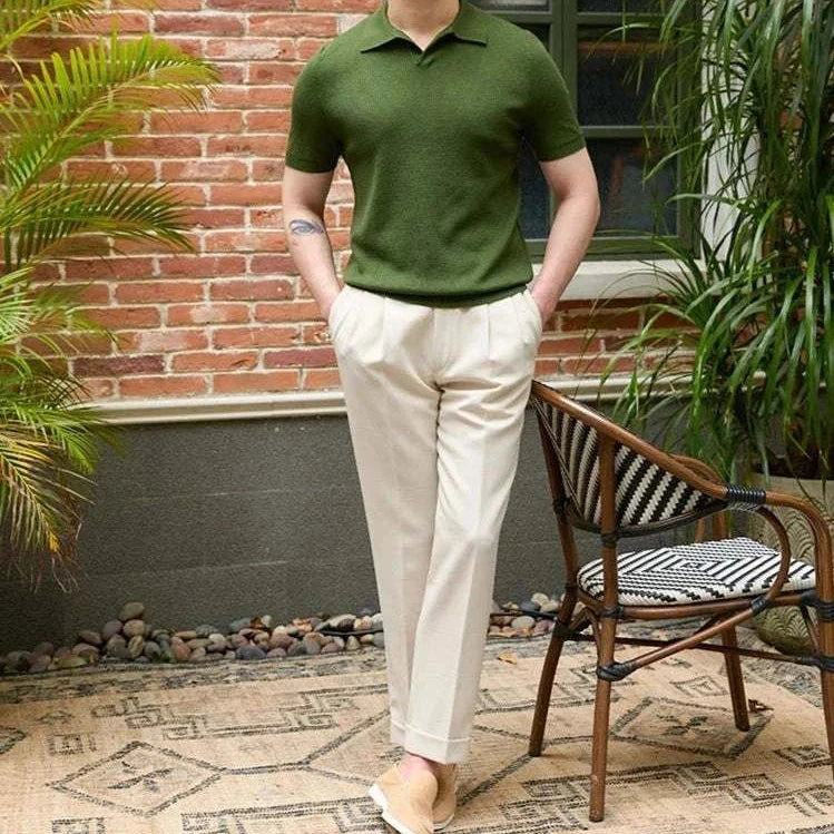 Man wearing a summer v-neck polo English t-shirt in green with beige trousers, set in a stylish outdoor setting with plants.