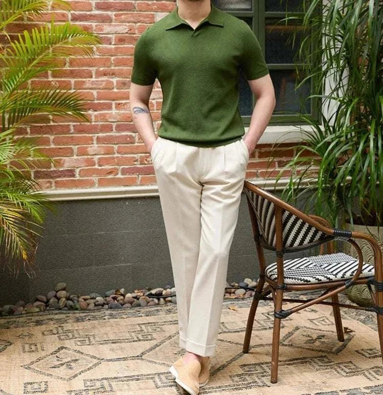 Man wearing a summer v-neck polo English t-shirt in green with beige trousers, set in a stylish outdoor setting with plants.
