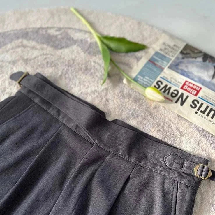 High waist gentleman trousers in dark fabric with leaf and newspaper on textured background.
