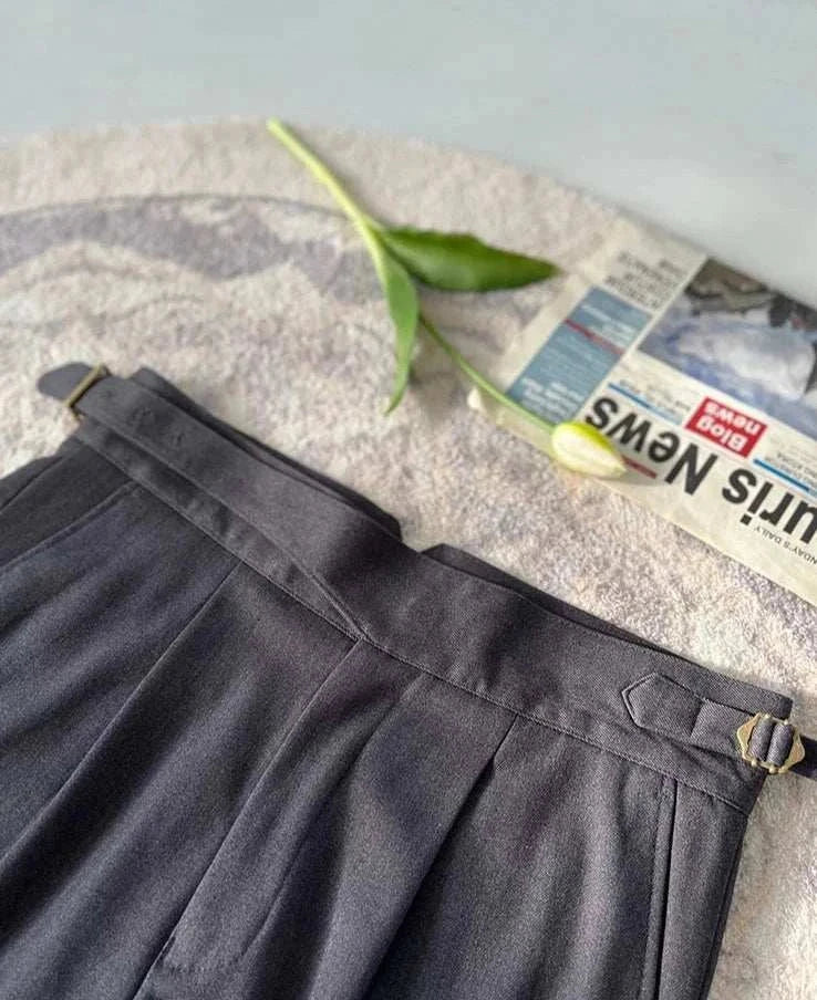 High waist gentleman trousers in dark fabric with leaf and newspaper on textured background.