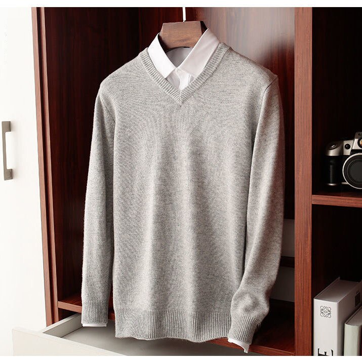 Men's light gray V-neck sweater hanging in a wooden wardrobe, featuring a solid pattern and made of wool blend for warmth and comfort.