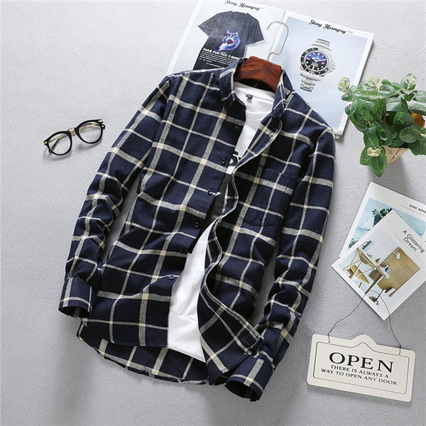 Men's long sleeve plaid shirt on table with eyewear and magazines.