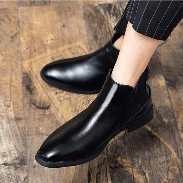 Black leather boots on wooden floor, worn with pinstripe pants.