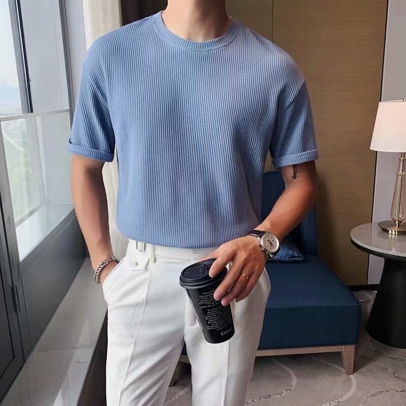 Man wearing Antonios Round Collar Short Sleeve T-shirt in blue, made of 100% organic cotton, styled with white pants in a casual setting.