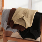 Four textured blankets in gray, brown, beige, and black draped over a wooden chair.