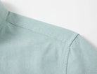 Close-up detail of a light sage green shirt showing the shoulder seam, collar, and fabric texture against a plain white background.