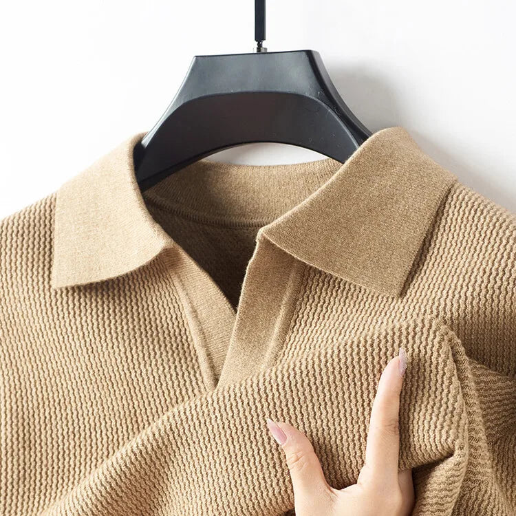 Beige textured sweater on a hanger with a hand touching the fabric
