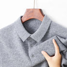 A close-up of a gray knit polo shirt hanging on a wooden hanger, with a hand holding the sleeve to show the fabric texture against a plain white background.