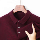 A close-up of a burgundy knit polo shirt on a wooden hanger, with a hand holding the sleeve to show the fabric texture.
