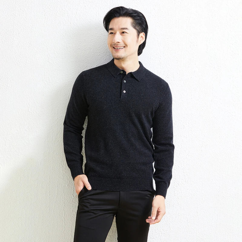 A man wearing a dark charcoal knit polo shirt and black pants, standing against a light textured wall.