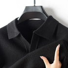 Black knit sweater on a hanger with a hand touching the fabric