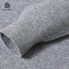 Close-up of a gray ribbed knit sleeve cuff with a heathered gray fabric body, showing texture and a small '100% WOOL' logo in the upper left corner.