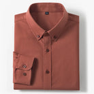 A folded long-sleeve button-down shirt in a muted terracotta or rust color, displayed on a clean white background.
