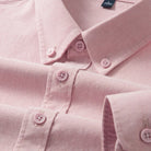 A close-up of a light pink long-sleeve button-down shirt, showing the collar, button details, and fabric texture.