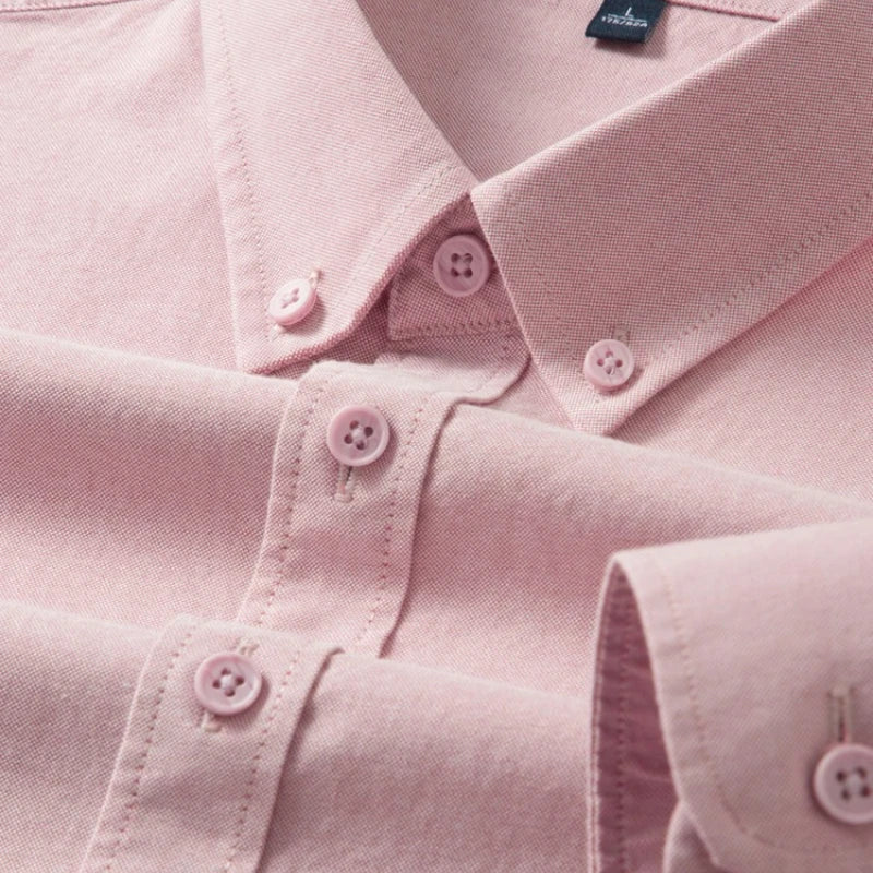 A close-up of a light pink long-sleeve button-down shirt, showing the collar, button details, and fabric texture.
