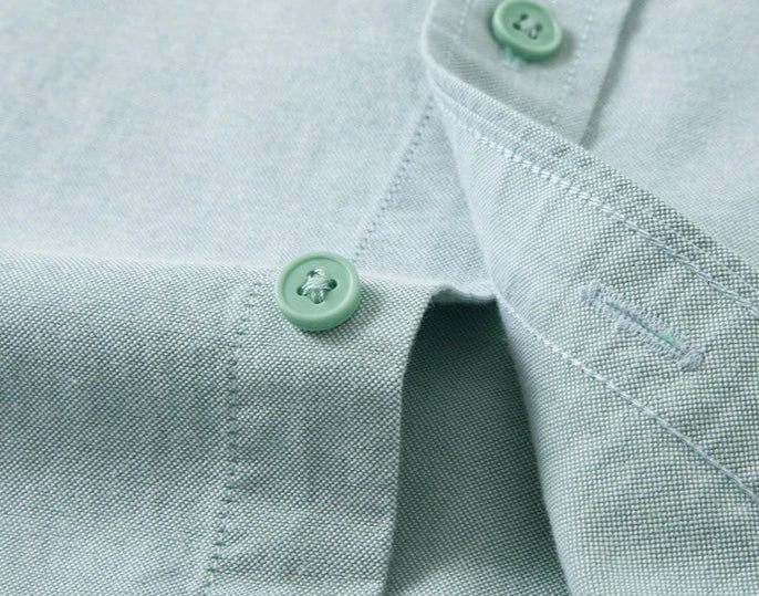 Close-up of a light sage green woven fabric garment, showing the collar, button placket, and matching green buttons.
