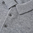 Close-up of a gray heathered wool polo shirt showing the collar, button placket, and a small '100% WOOL' logo in the top-left corner.