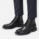 Leather wingtip boots with side zips in black, side view on a model